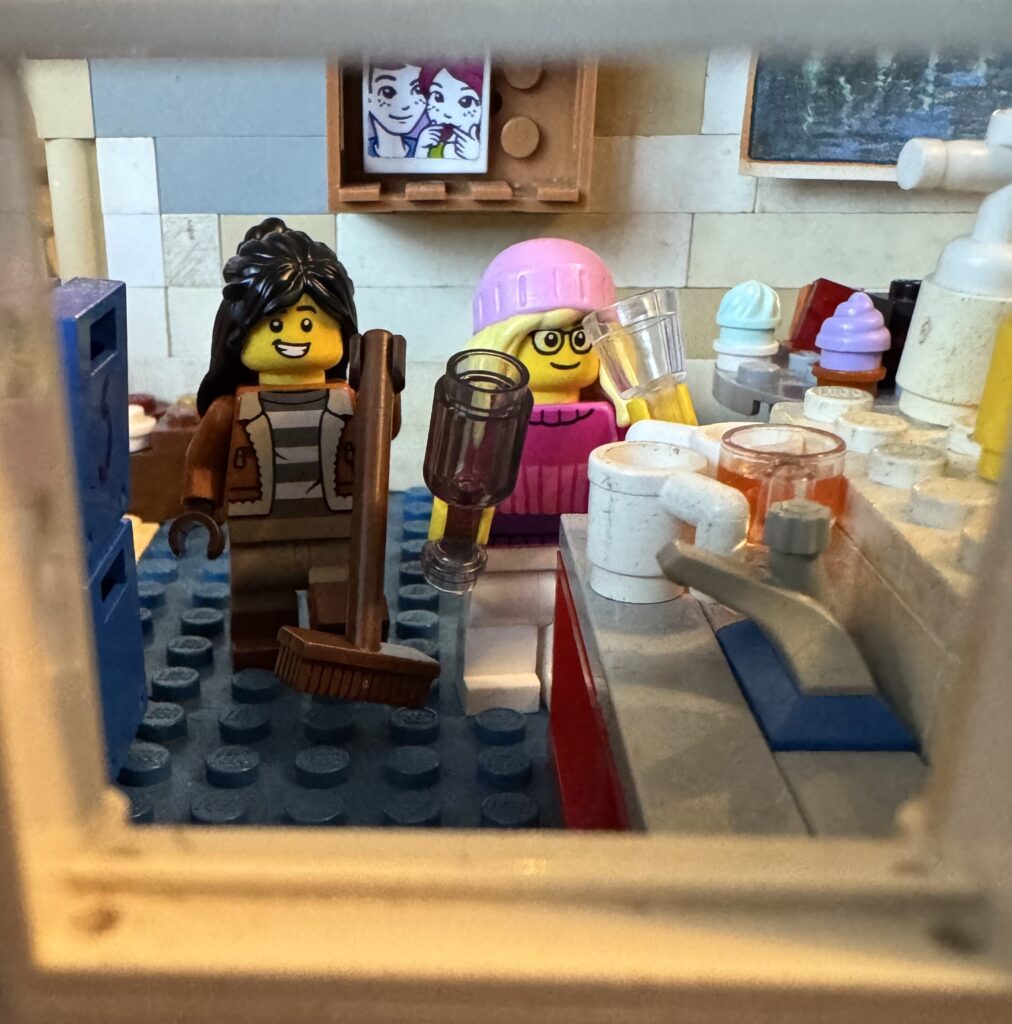 Fay en Jip druk bezig in de keuken. Jip is aan het vegen en Fay zet glazen op het aanrecht