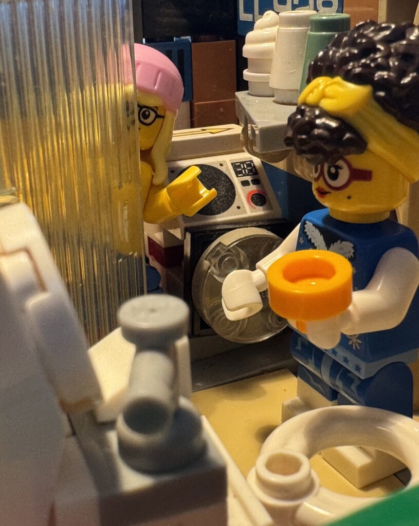 Wapke en Fay in de badkamer. Wapke heeft een potje vast en Fay kijkt om het hoekje van de douchedeur.